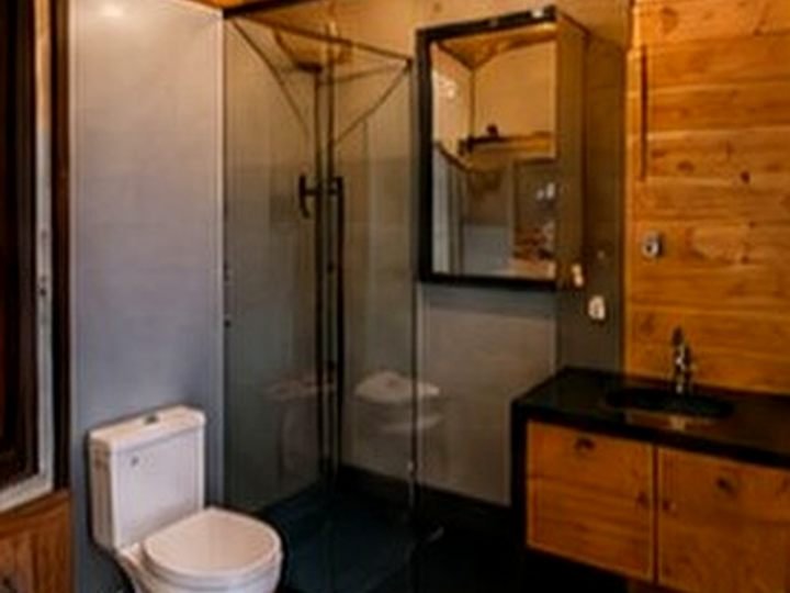 Banheiro do chalé com box de vidro, gabinete de madeira e revestimento em ACM