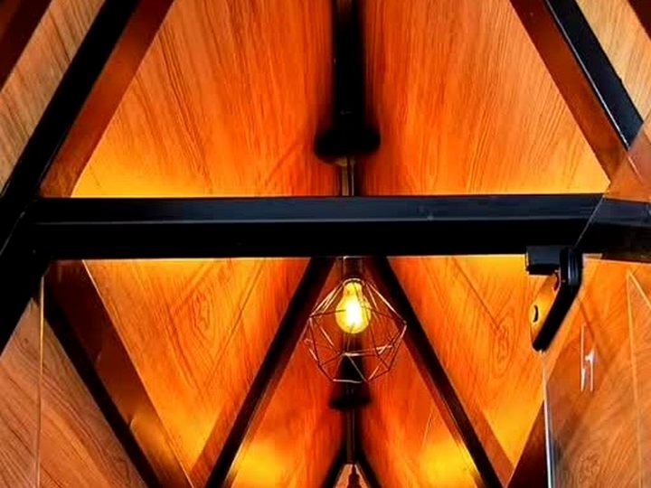 Interior do chalé A-frame com forro em PVC amadeirado e luminárias aramadas